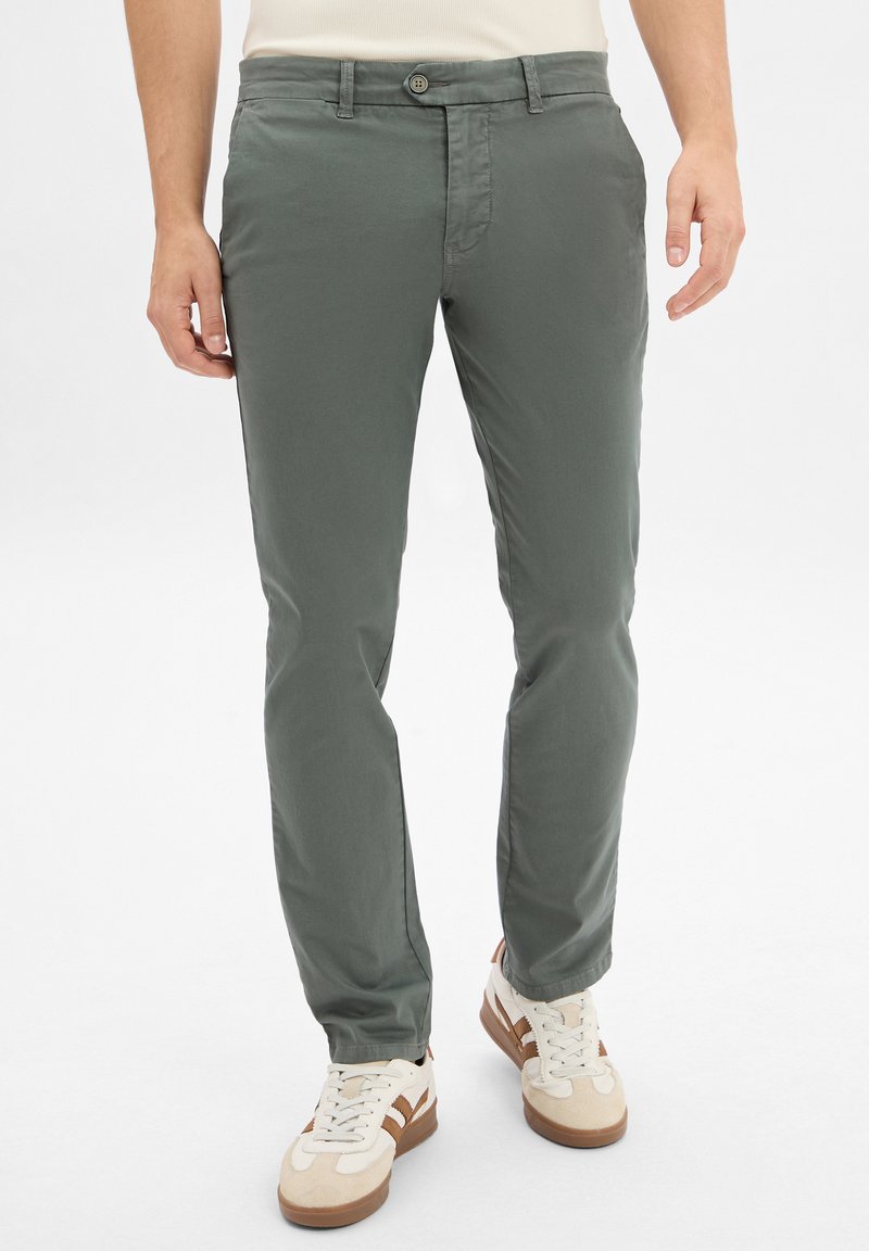 Męskie jasnoszare chinosy wykonane z miękkiej tkaniny. Posiadają zapięcie na guzik i kieszenie. Połączone z beżowymi i brązowymi trampkami.