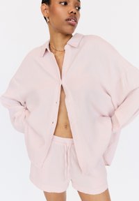 Lichtroze, gestructureerde, knoopshirt met een losse pasvorm en korte mouwen, gecombineerd met bijpassende shorts met een elastische taille en trekkoord.