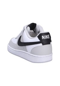 Baskets Nike blanches et grises avec logo swoosh noir et languette de talon noire affichant le nom de la marque Nike, vues de l'arrière droit.