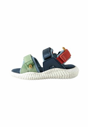 Sandale sportive pour enfant avec semelle épaisse blanche tachetée, brides réglables vertes, bleu marine et rouges, vue de côté sur fond blanc.