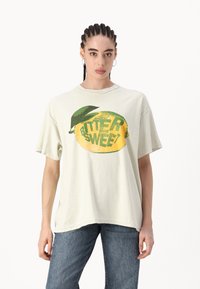 Camiseta oversized verde claro, con un gran gráfico de limón amarillo con acentos verdes y el texto "AMARGO DULCE". Textura suave, diseño casual.