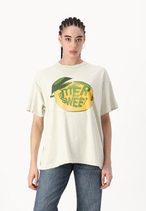 Light green oversized t-shirt, featuring a large yellow lemon graphic with green accents and the text “BITTER SWEET.” Soft texture, casual design.