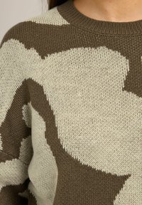 Sweter dzianinowy w kolorze kremowym i oliwkowym z dużym abstrakcyjnym wzorem. Żebrowany kołnierz i zbliżenie na teksturowany materiał. Wygodny i luźny krój.