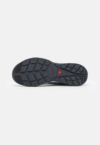 Shoe sole featuring black rubber material with deep treads and a red accent; textured for grip and stability.