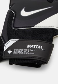 Guanti da calcio neri con materiale texturizzato, accenti bianchi e una fascia etichettata "MATCH JR" con ulteriori dettagli sul prodotto.