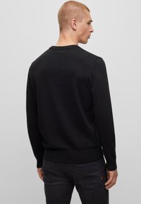 Maglione nero a collo rotondo con maniche lunghe, polsini e orlo a coste. Texture liscia, design minimalista, indossato con jeans scuri.