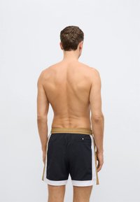 Pánske plavkové šortky v čiernej, zlatej a bielej farbe. Majú šnúrku v páse na stiahnutie a zadnú kapsu. Materiál pôsobí ľahko a rýchloschnúco.