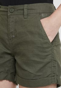 Olive green shorts with a button closure, front pockets, and rolled hems. Made from a soft, textured fabric with contrasting stitching.