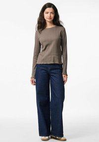Maglietta a maniche lunghe marrone con costine e orlo a scallop, abbinata a jeans a gamba larga blu scuro. Texture morbida e vestibilità rilassata.