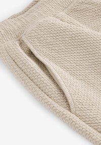 Tissu beige texturé avec un motif tissé, doté d'un bord doux et nervuré à l'ourlet. La surface a une qualité tactile légèrement surélevée.