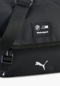 Fekete üzenetküldő táska állítható pánttal, BMW Motorsport logóval és fehér Puma logóval. Tartós szövetből készült, sima textúrával.