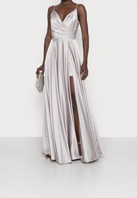 Vestito lungo in satin grigio chiaro con scollatura a V profonda, vita plissettata e spacco alto fino alla coscia. Modella che tiene una piccola clutch grigia.