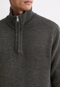 Grau gestreifter Halb-Reißverschluss-Pullover mit hohem Kragen. Der Stoff weist entlang der vertikalen Linien eine gerippte Textur auf. Silberner Reißverschluss als Detail am Kragen.