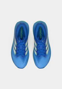 Μπλε αθλητικά παπούτσια με υφασμάτινο πάνω μέρος με υφή, πάνελ από δίχτυ, τρεις λευκές ρίγες και πράσινες λεπτομέρειες στη σόλα. Τα παπούτσια έχουν στρογγυλεμένη μύτη.