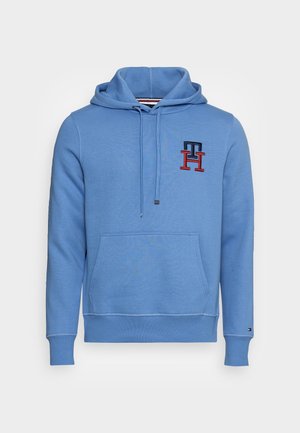 Sudadera con capucha azul claro hecha de tela suave, con bolsillo frontal, capucha con cordón, y logo bordado en azul oscuro y rojo.