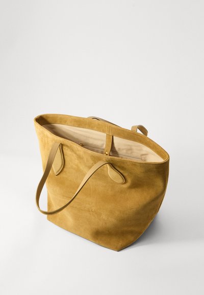 Sac fourre-tout en suede jaune avec une large ouverture, deux poignées et un intérieur beige comprenant un compartiment zippé et des détails cousus.