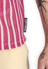 Roze en crème gestreepte gebreide top met een gestructureerd patroon, voorzien van een zijlabel. Lichte stof is zichtbaar onder de top.