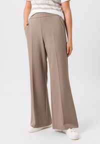 Beige wijde broek met een gladde structuur, voorzien van voorzakken en een hoge tailleband. Gecombineerd met witte sneakers voor een casual look.