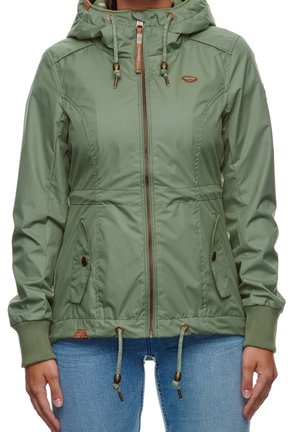 Vrouw draagt lichtgroene zip-up jas met capuchon, trekkoorden en met knopen gesloten klepzakken, gecombineerd met blauwe spijkerbroek.