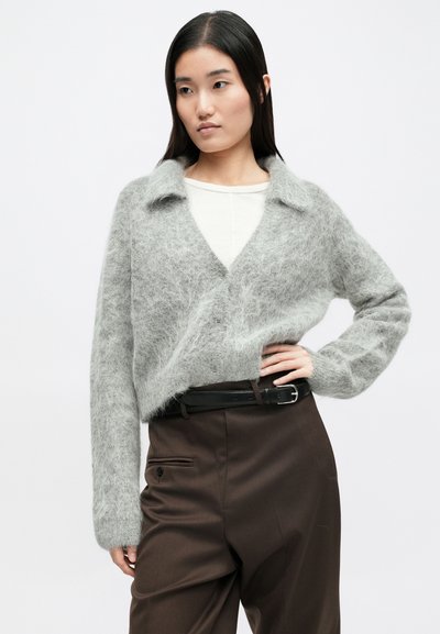 Szary, puszysty kardigan z kołnierzem typu szal, zapinany na guziki, z długimi rękawami, noszony na lekkiej bluzce, w zestawieniu z ciemnymi, dopasowanymi spodniami.