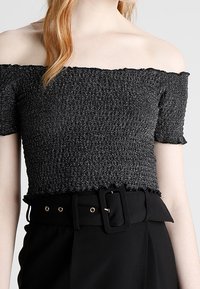 Czarna bluzka na ramiączkach z fakturowanej tkaniny, krótki rękaw i falbaniasty dół. W zestawie z czarnym paskiem z prostokątną klamrą.