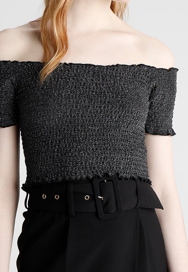 Czarna bluzka na ramiączkach z fakturowanej tkaniny, krótki rękaw i falbaniasty dół. W zestawie z czarnym paskiem z prostokątną klamrą.