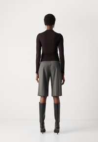 Fitted black long-sleeve top paired with high-waisted, knee-length gray shorts. Black knee-high boots complete the outfit.