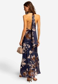 Maxikleid mit navy Hintergrund, mit einem floralen Muster in Beige und Braun, im Halterneck-Design und einem offenen Rücken.