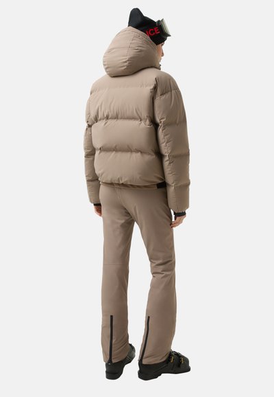 Beżowa kurtka puchowa z kapturem, teksturowanymi panelami i dopasowanymi rękawami, zestawiona z pasującymi beżowymi spodniami z zamkami błyskawicznymi przy kostkach.