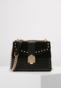 Czarna torebka wykonana ze skóry i zamszu, z złotymi ćwiekami, z klapą na zapięcie i łańcuszkowym paskiem. Prosta konstrukcja z geometrycznymi akcentami.