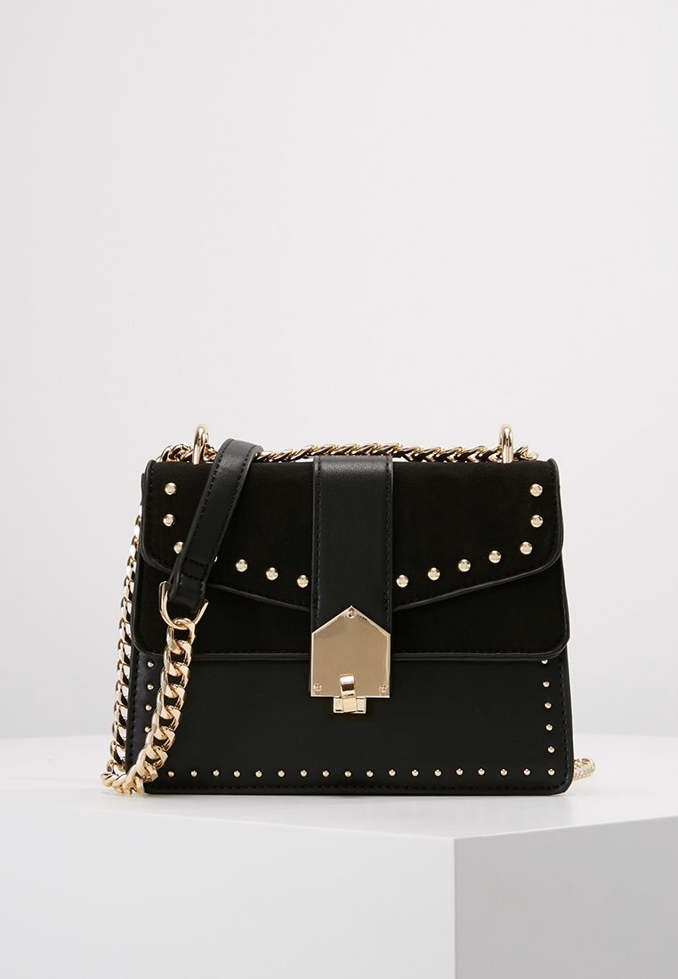 Czarna torebka wykonana ze skóry i zamszu, z złotymi ćwiekami, z klapą na zapięcie i łańcuszkowym paskiem. Prosta konstrukcja z geometrycznymi akcentami.