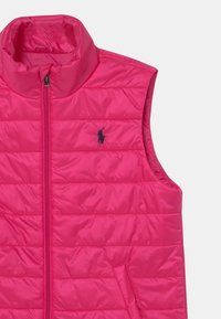 Rosa pufferväst med hög krage, vertikalt quiltat mönster och en liten svart logotyp på vänster bröst. Lättvikts- och ärmlös design.