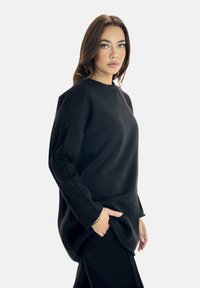 Felpa nera oversize con maniche lunghe, scollatura rotonda e tasche laterali, realizzata in un tessuto morbido e testurizzato. Design semplice, senza motivi.