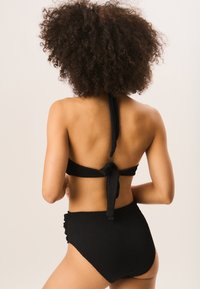 Black bikinis with a textured fabric, halter neck design, and tied back. High-waisted bottoms feature side ruching details.