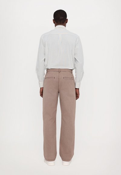 Light blue and white striped long-sleeve shirt, paired with loose-fitting beige pants. Visible back pockets on pants, minimalistic design.