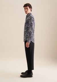 Camicia a maniche lunghe a fantasia con design floreale in blu scuro e bianco, abbinata a pantaloni neri e scarpe nere. Trame di tessuto lisce.