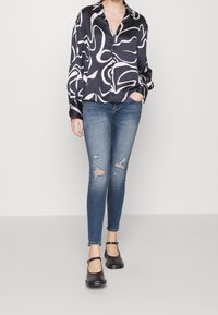 Camisa de satén de manga larga con un patrón abstracto en blanco y negro, combinada con jeans pitillo azules desgastados y zapatos Mary Jane negros.