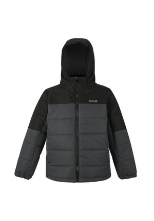 Niño con una chaqueta acolchada negra y gris con capucha, de pie y mirando ligeramente hacia un lado con una leve sonrisa.