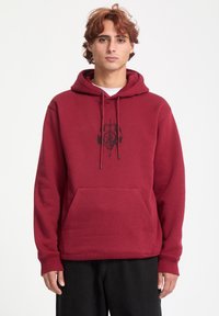 Sudadera burdeos con un bolsillo frontal y diseño gráfico negro. Cuenta con capucha ajustable con cordón y puños y dobladillo de canalé. Material suave de mezcla de algodón.
