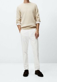 Beiger strukturiert Pullover mit Rundhalsausschnitt, kombiniert mit weißen geraden Hosen und dunkelbraunen Schuhen. Einfaches Design, minimale Akzente.