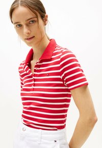 Rood-wit gestreepte polo shirt met een kraag, voorzien van een drieknopen placket en een logo op de borst, gecombineerd met witte broek.