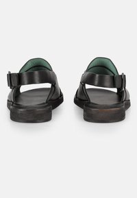 Sandali in pelle nera con rivestimento interno verde, cinturino alla caviglia regolabile, suola piatta e design aperto sul retro. Texture morbida con dettagli minimi.