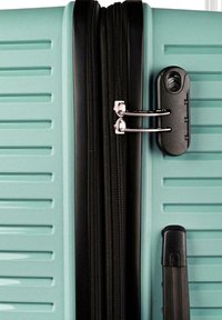 Maleta rígida de color verde azulado claro con doble cremallera asegurada con un candado de combinación negro junto a un asa negra.