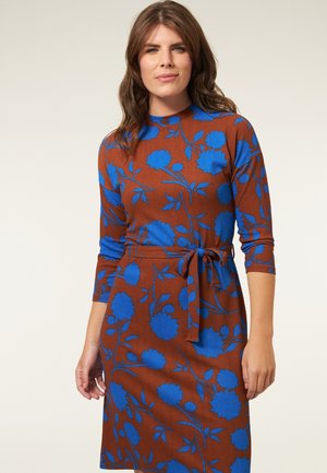 Bruine jurk met een blauw bloemenpatroon, driekwart mouwen, hoge halslijn, een gestrikt tailleband en een rechte snit. Getextureerde stof.