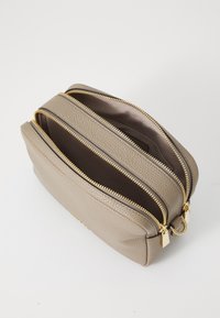 Trousse de toilette en cuir beige avec trois compartiments zippés, accents en matériel doré, surface texturée et un intérieur spacieux.