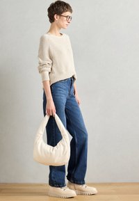 Suéter de punto beige, jeans de mezclilla azul, bolso hobo crema, zapatos de plataforma crema con suelas texturizadas, detalles sutiles de puños elásticos.