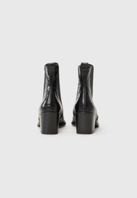 Bottes noires en cuir à la cheville avec une texture brillante en relief crocodile et un talon carré. Design simple avec des accents minimalistes, vue arrière présentée.
