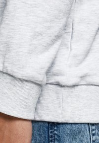 Tessuto grigio del sudore con una consistenza morbida e polsini a coste. Il tessuto presenta un leggero motivo melange, mescolando grigio chiaro e scuro.