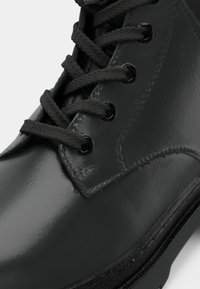 Czarny, błyszczący botek za kostkę z fakturowanym czarnym sznurówkami, metalowymi oczkami i zaokrąglonym noskiem. Gładka cholewka i trwała gumowa podeszwa.