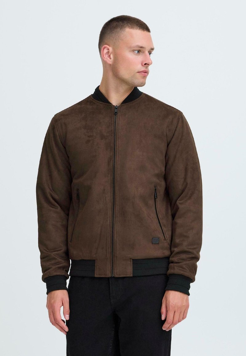 Braune Wildleder-Bomberjacke mit einem schwarzen gerippten Kragen und Bündchen, ausgestattet mit zwei seitlichen Reißverschlusstaschen und einem Reißverschluss vorne.